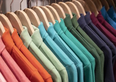 Mağazada asılı renkli polo tişört. Ahşap askıda yeşil mavi polo. Alışveriş merkezinde yaz mevsimi giysisi. Sıcak hava için erkek kıyafeti. Alışveriş merkezinde indirim var. Yakalı örgü gömlek.