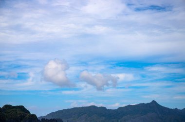 Mavi gökyüzü ve dağlardaki bulutlar. Tropik ada silueti. Tropik bulutsu fotoğrafı. Mavi gökyüzünde kabarık bulut