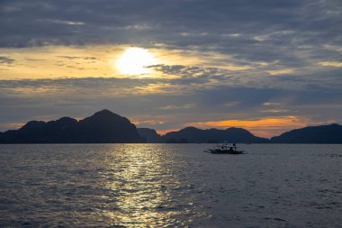 Uzak dağlar ve tekne ile bulutlu sahil manzara. Gün batımı ile romantik akşam deniz manzarası