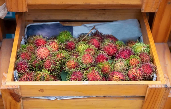 Tropical fruit rambutan in wooden box. Exotic fruit on organic market in Asian village. Fruit season in Asia.