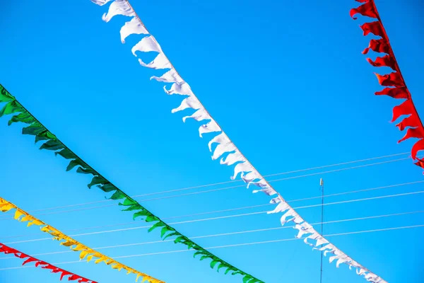 Colorful flag ribbons in sunny blue sky. Festival flag decor. Summer day outdoor. Optimistic skyscape with triangle ribbon.