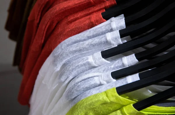 Разноцветная верхняя одежда висит в магазине моды. Красная, белая и желтая текстильная рубашка на черной вешалке . — стоковое фото