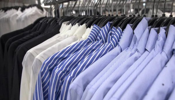 Vit och blå skjorta till salu i butik. Manligt slitage på plastgalge. Officiella kläder för män i varuhuset — Stockfoto