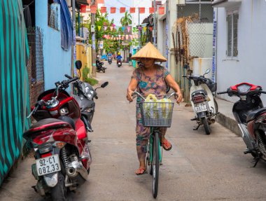 Hoi An, Vietnam - 28 Temmuz 2019: Dar yolda bisiklet süren geleneksel Vietnam şapkalı kadın.
