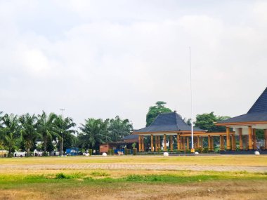Tranquil morning view of park with traditional buildings, palm trees, and a clear, bright sky