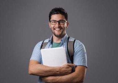 Holding beyaz ders kitabı ve sırt çantası onun omzuna gözlük ile kıl, genç gülümseyen öğrenci portresi