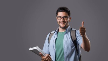 Omzunda jest ve sırt çantası yukarı gösteren gözlük beyaz ders kitabı, holding kıl ile genç gülümseyen öğrenci portresi