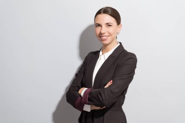 Genç gülümseyen güzel görünümlü iş kadını gri arka plan karşı çapraz kolları olan. Moda stil photoshoot zor ışık kaynağı ile