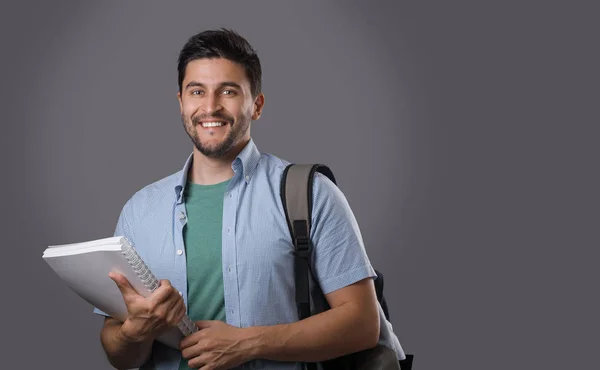 Holding beyaz ders kitabı ve sırt çantası onun omuz üzerinde kıl ile genç gülümseyen öğrenci portresi