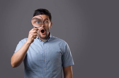 Genç sakallı adam gözünü büyütmek büyüteç ile hayran. Genç adam arama