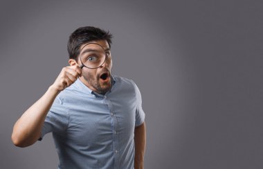 Genç sakallı adam gözünü büyütmek büyüteç ile hayran. Genç adam arama