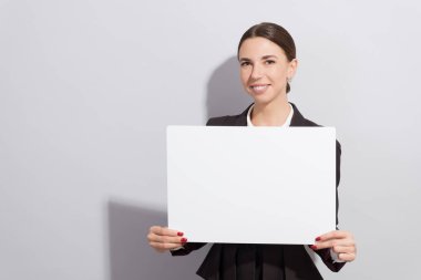 Boş poster gri arka plan üzerinde tutan genç gülümseyen iş kadın. Moda stil photoshoot zor ışık kaynağı ile