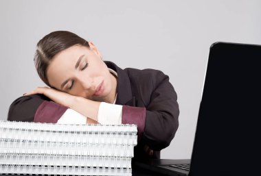 Genç iş kadını çalışma kağıtları ve Kitaplar ile laptop ile masaya oturan duraklama alarak yorgun. Ofiste zor iş akışı