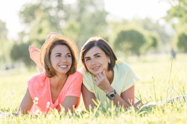 İki sevimli, çim yeşil park güneşli sıcak gün yatan kızlar gülüyor. Açık zaman yaz gün harcama