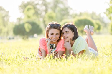 Açık çim üzerinde yalan, smartphone kullanarak ve iyi birlikte parkta güneşli gün vakit iki neşeli kız portresi.