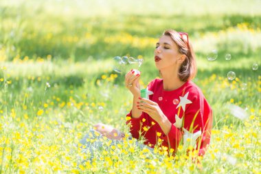 Çimenlerin üzerinde oturan ve sabun köpüğü hava güneşli gün parkta üfleme genç yakışıklı kız