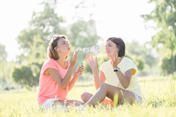 Retrato Aire Libre Dos Chicas Alegres Sentadas Césped Soplando Burbujas —  Fotos de Stock