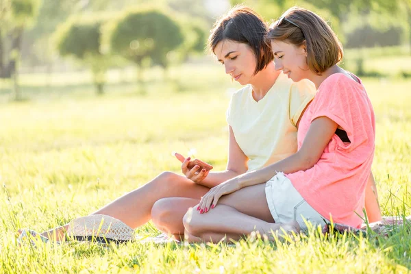 Retrato Livre Duas Meninas Alegres Sentadas Gramado Usando Smartphone Divertindo — Fotografia de Stock
