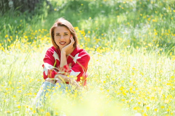 晴れた日に草の上に座って若いハンサムな女の子 公園で赤いセーターで陽気なリラックスした女性の屋外のポートレート — ストック写真