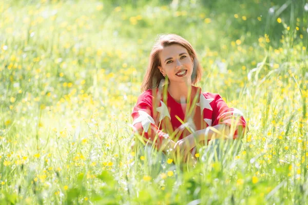 晴れた日に草の上に座って若いハンサムな女の子 公園で赤いセーターで陽気なリラックスした女性の屋外のポートレート — ストック写真