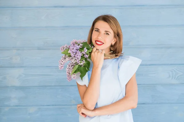 stock image Beautiful portrait of young charming girl with bouquet of fresh lilac against blue wooden background