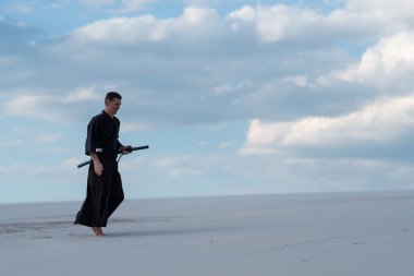 Dövüş sanatları uygulamak konsantre adam çölde bir Japon kılıç ile-geleneksel Japon kıyafetli bir katana yürür.