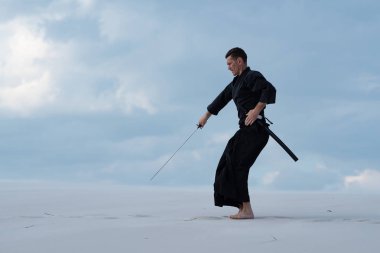 Geleneksel Japon giysili odaklı adam dövüş sanatları bir Japon kılıç - sunset akşam gökyüzü arka plan üzerinde sırasında bir katana ile çölde pratik.