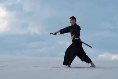 Geleneksel Japon giysili konsantre adam dövüş sanatları bir Japon kılıç - sunset akşam gökyüzü arka plan üzerinde sırasında bir katana ile çölde pratik.