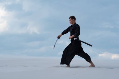 Geleneksel Japon giysili kararlı adam dövüş sanatları bir Japon kılıç - sunset akşam gökyüzü arka plan üzerinde sırasında bir katana ile çölde pratik.