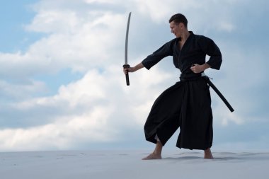 Geleneksel giysiler içinde odaklanmış adam Japon dövüş sanatları bir Japon kılıç - sunset akşam gökyüzü arka plan üzerinde sırasında bir katana ile çölde pratik.