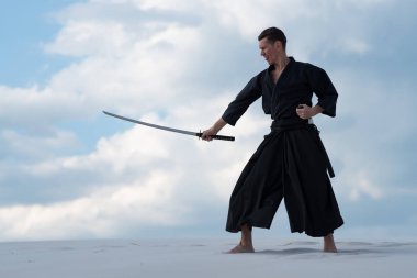 Geleneksel giysiler içinde odaklanmış adam Japon dövüş sanatları bir Japon kılıç - sunset akşam gökyüzü arka plan üzerinde sırasında bir katana ile çölde pratik.