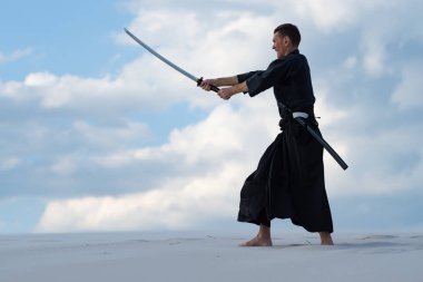 Geleneksel giysiler içinde odaklanmış adam Japon dövüş sanatları bir Japon kılıç - sunset akşam gökyüzü arka plan üzerinde sırasında bir katana ile çölde pratik.