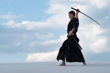 Geleneksel giysiler içinde odaklanmış adam Japon savaş sanatı - bir Japon kılıç ile çölde iaido - bir katana sunset akşam gökyüzü arka plan üzerinde sırasında pratik.