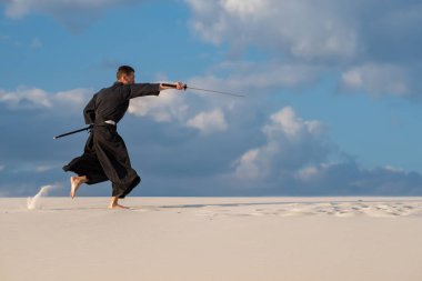 Geleneksel giysiler içinde kararlı adam Japon savaş sanatı - katana, bir Japon kılıç ile çölde iaido günbatımı gökyüzü akşam arka plan üzerinde sırasında pratik.