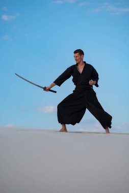 Odaklı kılıç, katana ile geleneksel Japon giysili adam, eğitim dövüş sanatları Çölü'nde Günbatımı - samuray mavi bulutlu gökyüzü arka plan üzerinde bulunuyor.