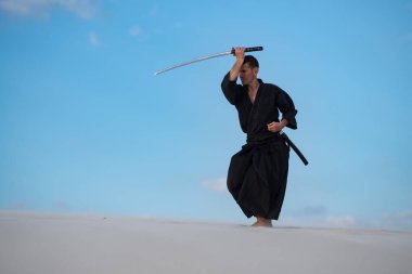 Odaklı kılıç, katana ile geleneksel Japon giysili adam, eğitim dövüş sanatları Çölü'nde Günbatımı - samuray mavi bulutlu gökyüzü arka plan üzerinde bulunuyor.