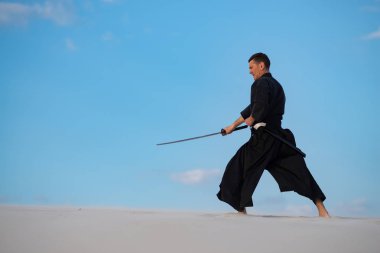 Odaklı kılıç, katana ile geleneksel Japon giysili adam, eğitim dövüş sanatları Çölü'nde Günbatımı - samuray mavi bulutlu gökyüzü arka plan üzerinde bulunuyor. Yan görünüm.