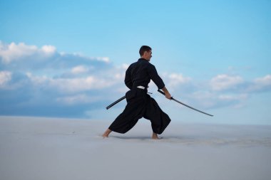 Odaklı kılıç, katana ile geleneksel Japon giysili adam, eğitim dövüş sanatları Çölü'nde Günbatımı - samuray mavi bulutlu gökyüzü arka plan üzerinde bulunuyor. Yan görünüm.