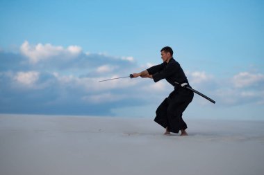 Odaklı kılıç, katana ile geleneksel Japon giysili adam, eğitim dövüş sanatları Çölü'nde Günbatımı - samuray mavi bulutlu gökyüzü arka plan üzerinde bulunuyor. Yan görünüm.