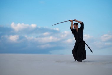 Odaklı kılıç, katana ile geleneksel Japon giysili adam, eğitim dövüş sanatları Çölü'nde Günbatımı - samuray mavi bulutlu gökyüzü arka plan üzerinde bulunuyor. Yan görünüm.