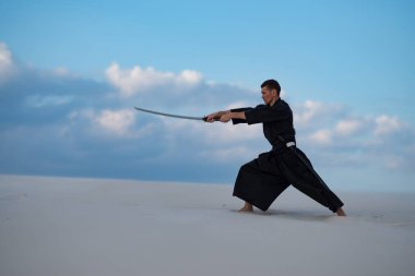 Odaklı kılıç, katana ile geleneksel Japon giysili adam, eğitim dövüş sanatları Çölü'nde Günbatımı - samuray mavi bulutlu gökyüzü arka plan üzerinde bulunuyor. Yan görünüm.