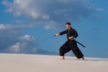Kararlı adam kılıçla, katana, geleneksel Japon elbiseleri günbatımı - samuray bulutlu gökyüzü arka plan üzerinde eğitim dövüş sanatları çölde sırasındadır.