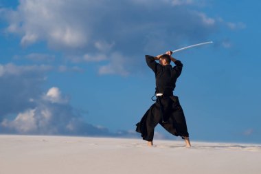 Kararlı adam kılıçla, katana, geleneksel Japon elbiseleri günbatımı - samuray bulutlu gökyüzü arka plan üzerinde eğitim dövüş sanatları çölde sırasındadır.