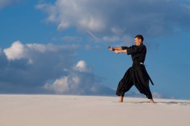 Kılıç, katana ile geleneksel Japon giysili adam, konsantre, eğitim dövüş sanatları Çölü'nde Günbatımı - samuray mavi bulutlu gökyüzü arka plan üzerinde bulunuyor.