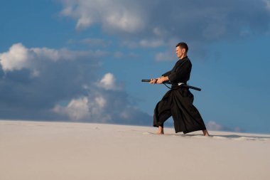 Konsantre, kılıçla, katana, geleneksel Japon giysili eğitim dövüş sanatları, iaido, günbatımı - samuray mavi bulutlu gökyüzü arka plan üzerinde sırasında çölde adamdır.