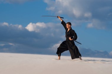 Kararlı adam kılıçla, katana, geleneksel Japon elbiseleri günbatımı - samuray bulutlu gökyüzü arka plan üzerinde eğitim dövüş sanatları çölde sırasındadır.