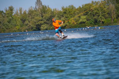 Wakeboarder, turuncu gömlek ve kask, güneşli bir günde bir kablo parkta eğitiyor. Açık içinde aktif bir tatil.