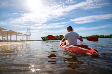 Bir güneşli sabah - su sporları tesisi üzerinde denizin plajın yanında bir kayık kürek çekmeye yetişkin adam. Arkadan görünüm, arka ışık, geniş açı.