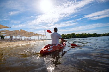 Bir güneşli sabah - su sporları tesisi üzerinde denizin plajın yanında bir kayık kürek çekmeye dostum. Arkadan görünüm, arka ışık, geniş açı.