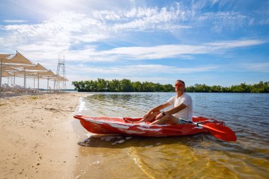 Bir kayık sonraki kumsala bir güneşli sabah - su sporları tesisi rahatlatıcı mutlu yetişkin adam. Geniş açı, arka aydınlatma.